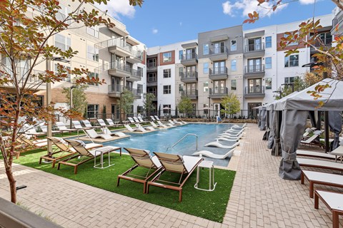 A pool surrounded by chairs and trees in front of apartment buildings.