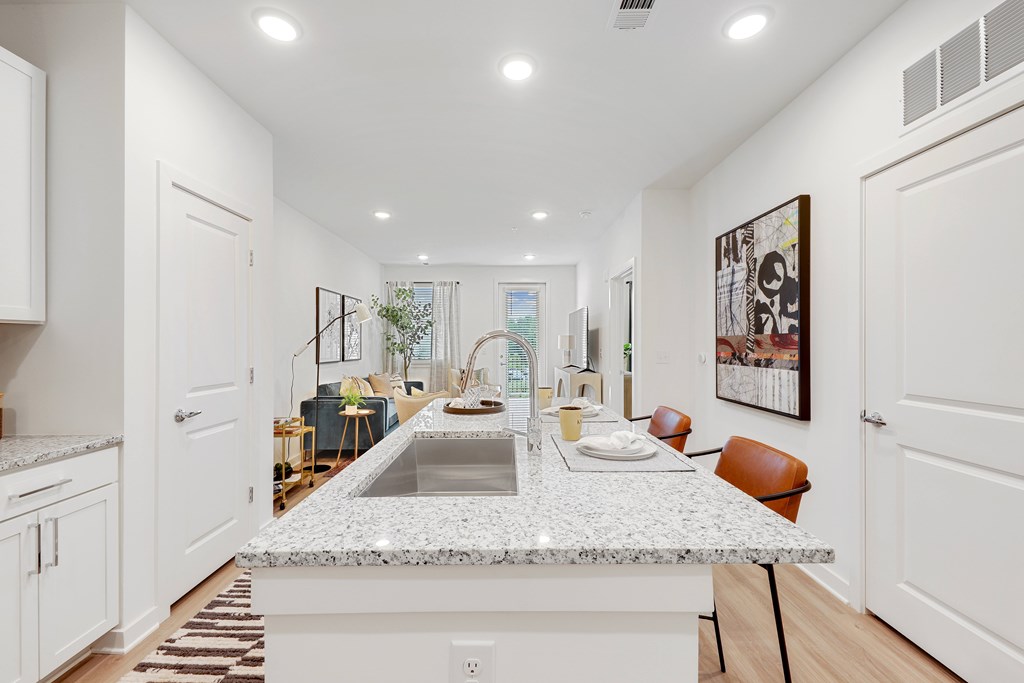 an open kitchen and living room with white cabinets and a granite counter top