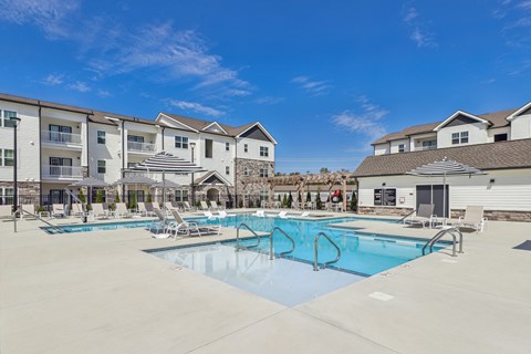 Two-Bedroom Apartments in Gallatin, TN - Banner at Westfield - Resort-Style Pool With Lounge Chairs, Shaded Umbrellas, And Apartment Buildings Under Blue Sky.