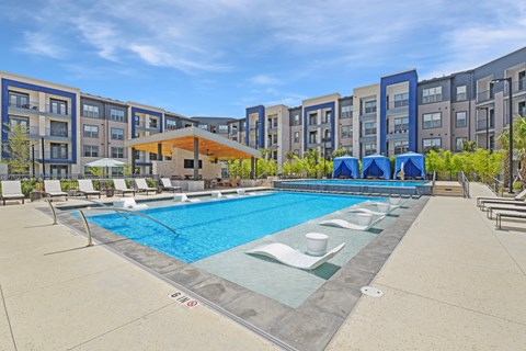 an outdoor pool with chairs and umbrellas and an apartment building in the background