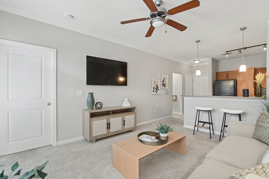 A living room with a white door, a flat screen TV, a wooden coffee table, and a beige couch.
