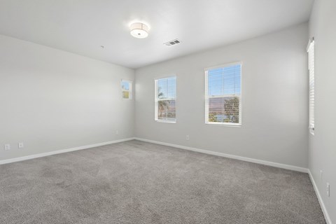 A spacious room with carpeted floor and two windows.