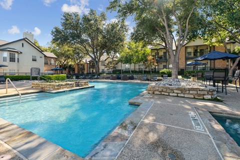 A swimming pool surrounded by trees and a stone border.