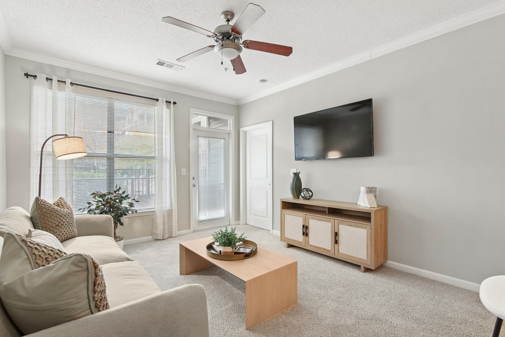 A living room with a couch, a coffee table, a television, and a fan.
