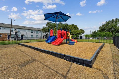 A playground with a slide, swings, and a blue umbrella.