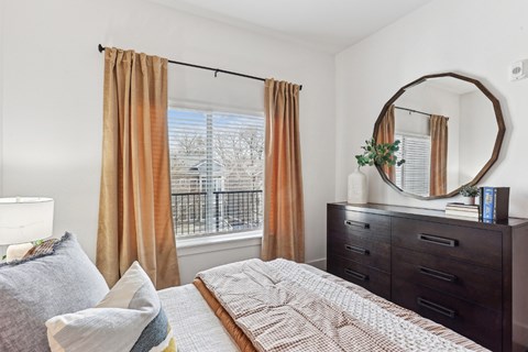 A bedroom with a large bed, a window with curtains, and a mirror on the wall.