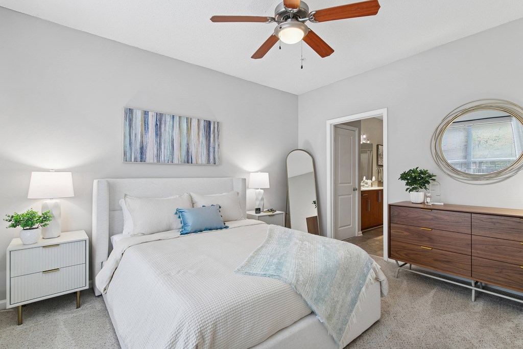 A bedroom with a large bed, a ceiling fan, and a mirror.