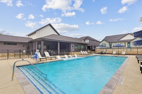 A large swimming pool with lounge chairs and a building in the background.
