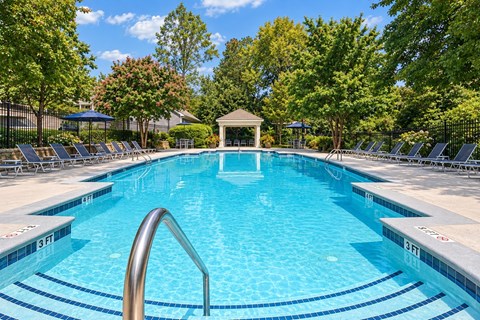 A swimming pool surrounded by trees and lounge chairs.
