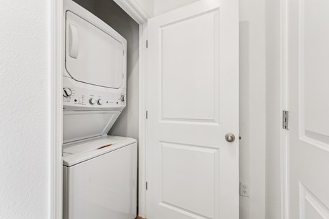 A white washing machine and dryer are in a small space between a door and a wall.