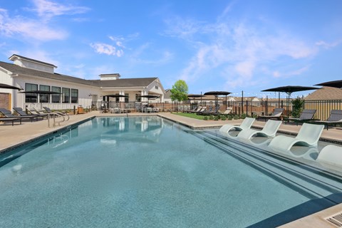 A large swimming pool with lounge chairs and a building in the background.