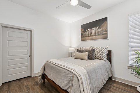 A bedroom with a bed, pillows, a ceiling fan, and a picture on the wall.