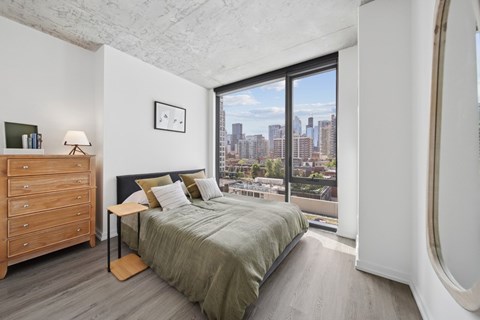 A bedroom with a bed, nightstand, and a window overlooking a cityscape.