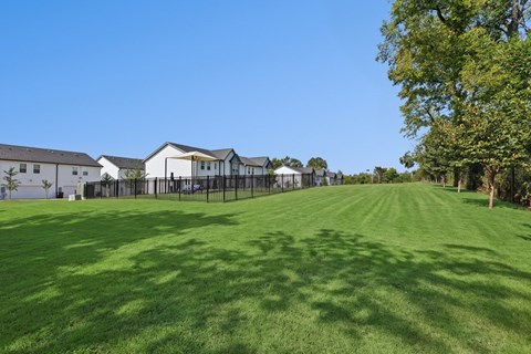 A large grassy field with a fence and buildings in the background.