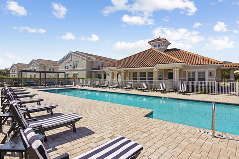 A pool with sun loungers and a building in the background.
