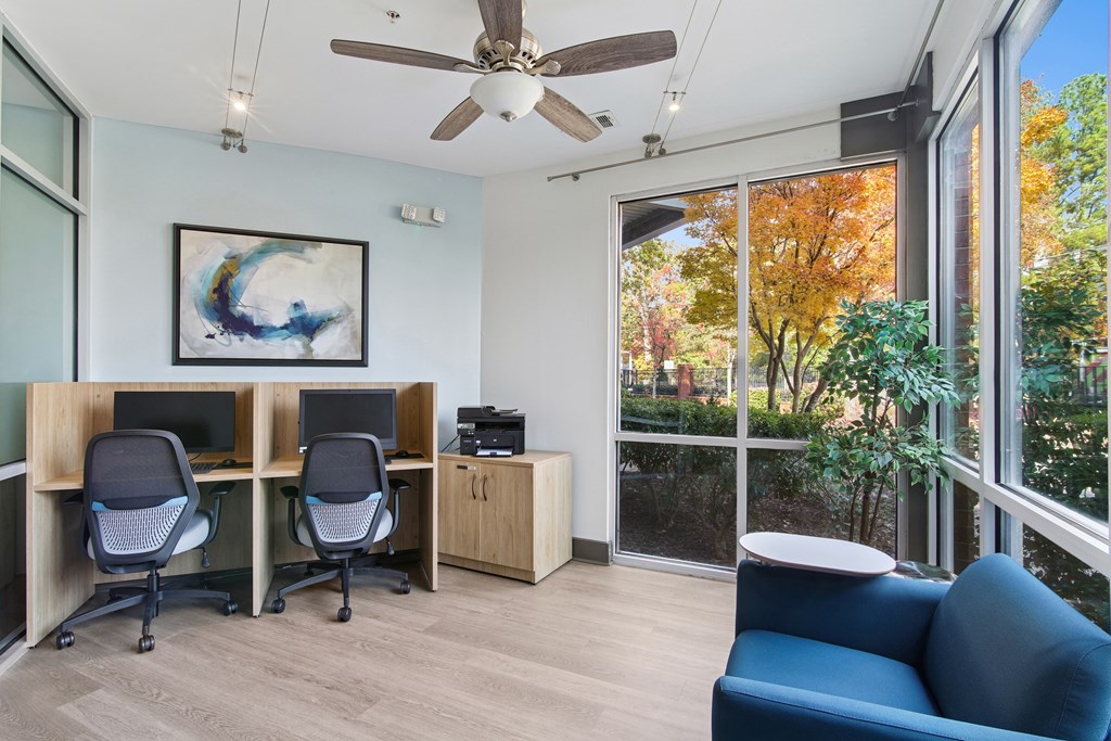A room with a ceiling fan, two chairs, a desk, and a painting.