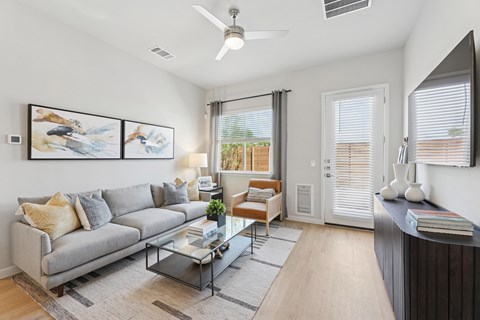 A living room with a grey sofa, a glass coffee table, and a painting on the wall.