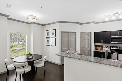 A kitchen with a table and chairs in the foreground and a countertop with a plant on it.