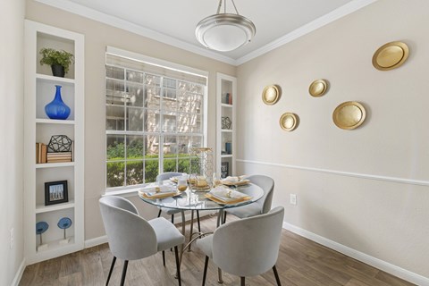 A dining room with a table set for two and a view of a tree outside the window.