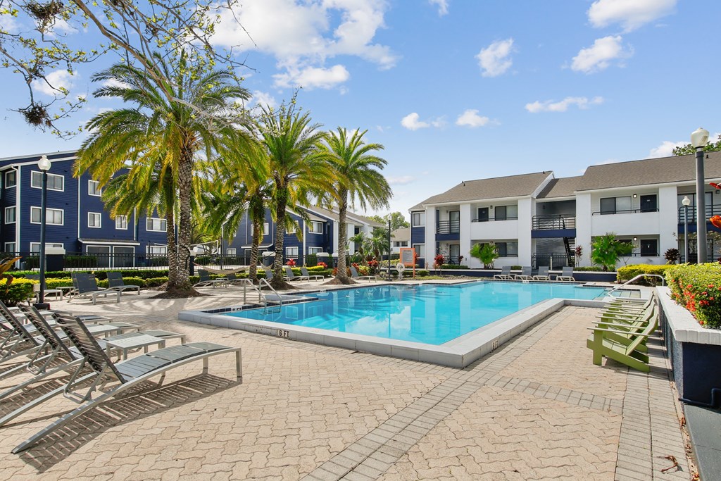 a swimming pool with chairs and palm trees in front of apartment buildings