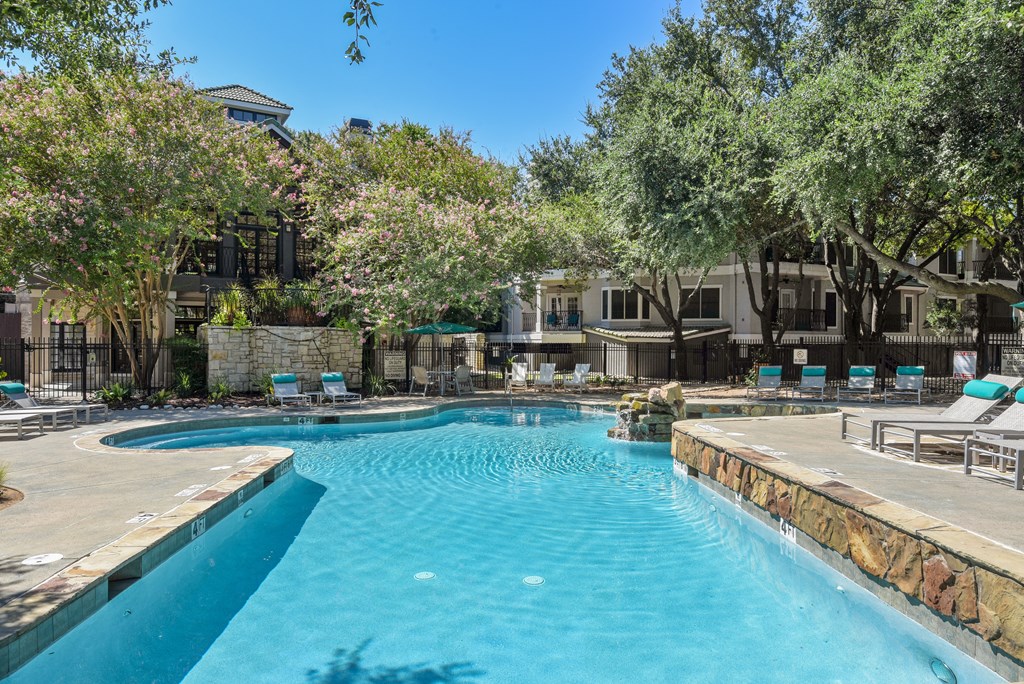 a swimming pool with lounge chairs and trees in the background