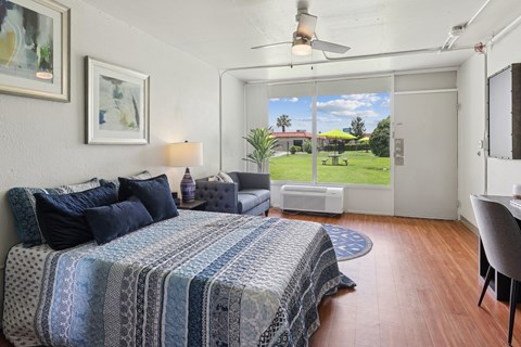 A bedroom with a bed, a chair, and a window overlooking a green lawn.