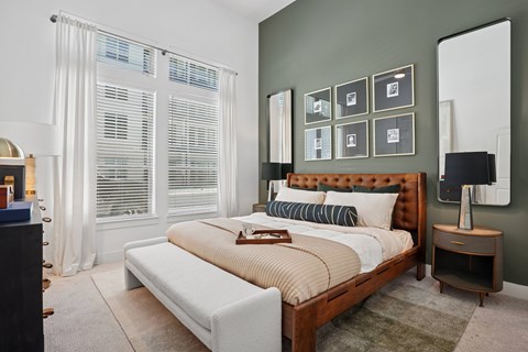 A bedroom with a large bed and a window with white curtains.