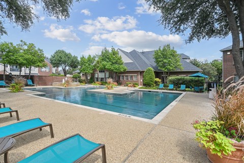 A pool surrounded by lounge chairs and trees.