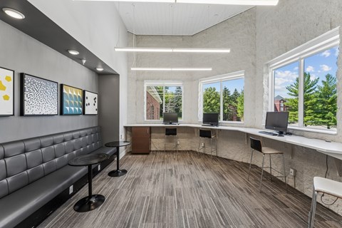 A room with a grey couch, a table, and a window with a view of trees and a building outside.