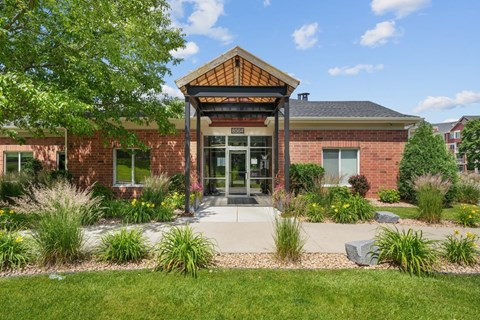 A building with a brick facade and a glass door is surrounded by greenery.
