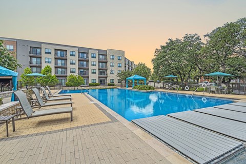 a swimming pool with chairs and umbrellas in front of an apartment building