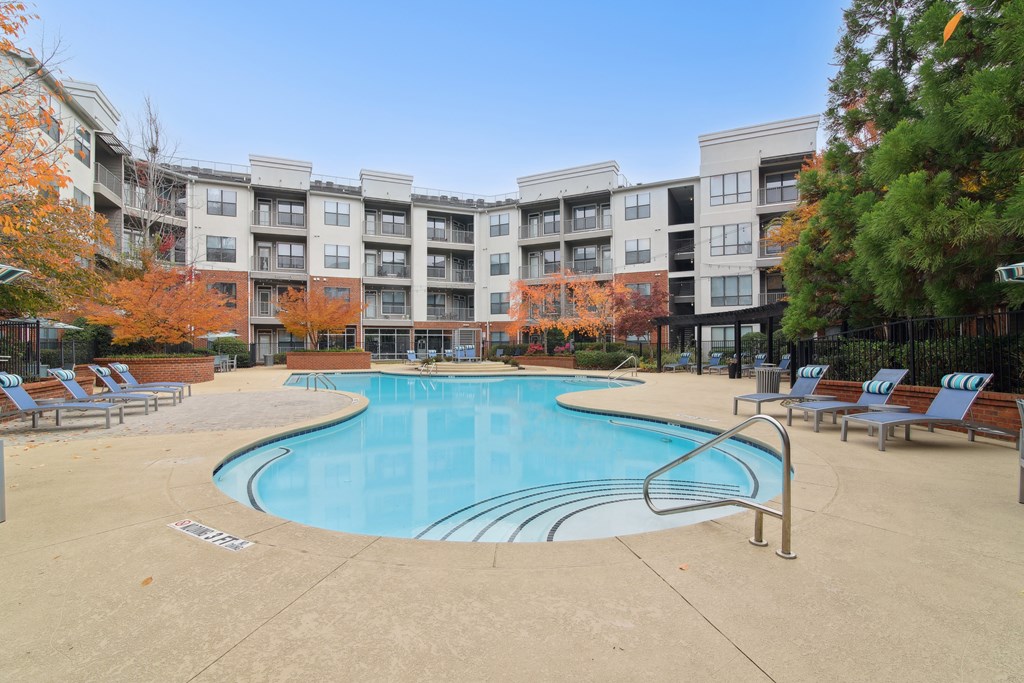 A swimming pool surrounded by chairs and trees in front of apartment buildings.