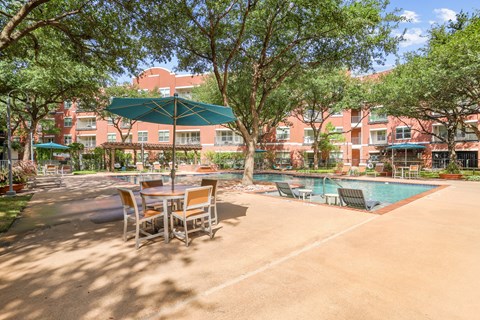 A pool area with a table and chairs and a green umbrella.