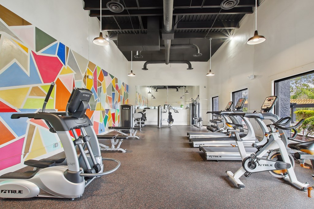 a gym with treadmills and weights and a colorful wall