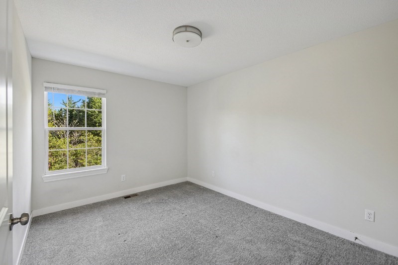 A room with a window and a smoke detector on the ceiling.