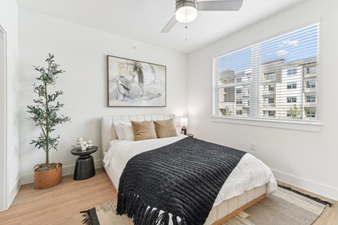 A bedroom with a bed, a ceiling fan, and a painting on the wall.