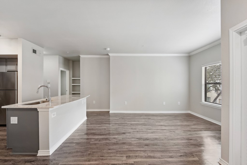 an empty living room with a kitchen and a large window