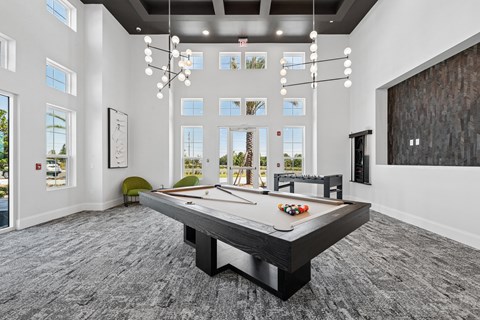 A pool table in a room with a high ceiling and large windows.