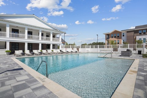 A large swimming pool in front of a white building with a poolside lounge area.