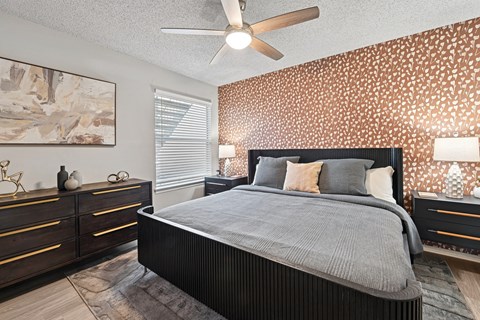 A bedroom with a large bed, a ceiling fan, and a painting on the wall.