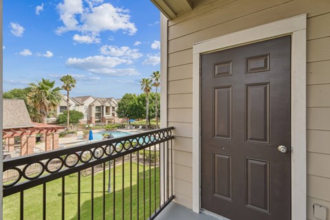 A balcony with a black railing and a brown door overlooks a pool and palm trees.