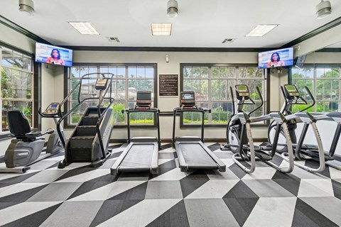 A gym with treadmills, exercise bikes, and a television screen.