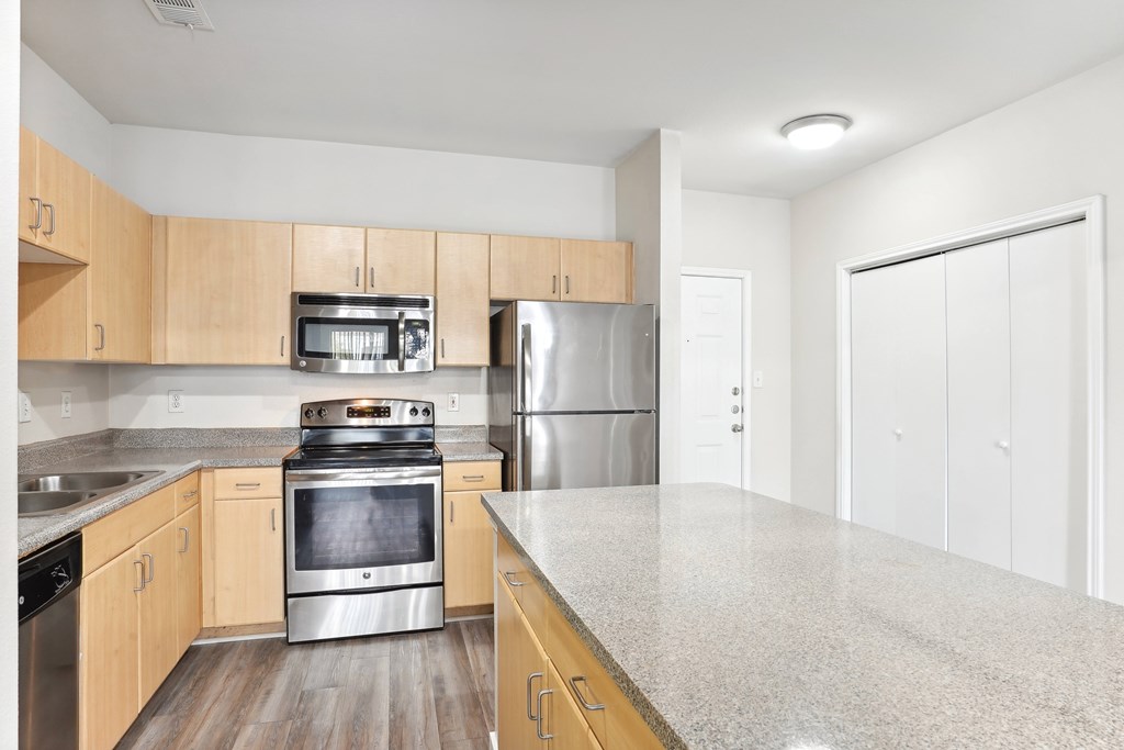 a kitchen with stainless steel appliances, pine color cabinets, hardwood style flooring and granite countertops