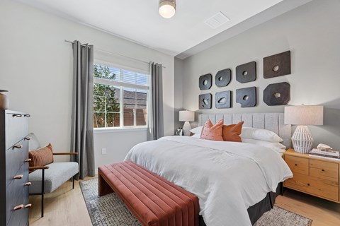 A bedroom with a large bed, a bench, and a window with curtains.