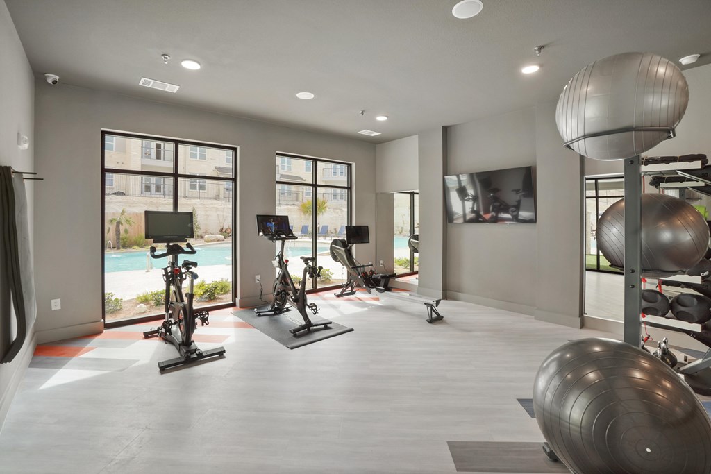 a spacious fitness room with cardio equipment and a large window with a view of the pool