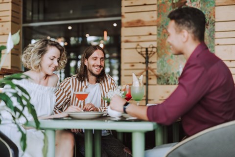 Three people are sitting at a table with drinks in front of a wooden wall.