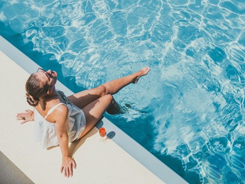A woman in a white top is sitting by a pool.