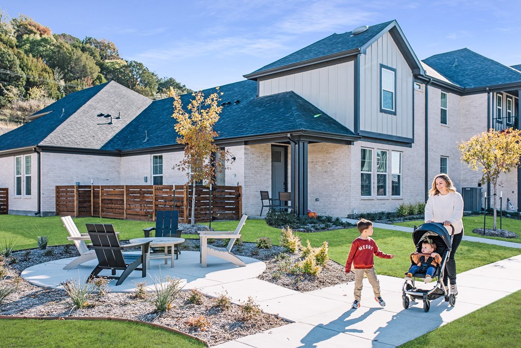 a mother pushing her child in a stroller on a backyard patio with a house