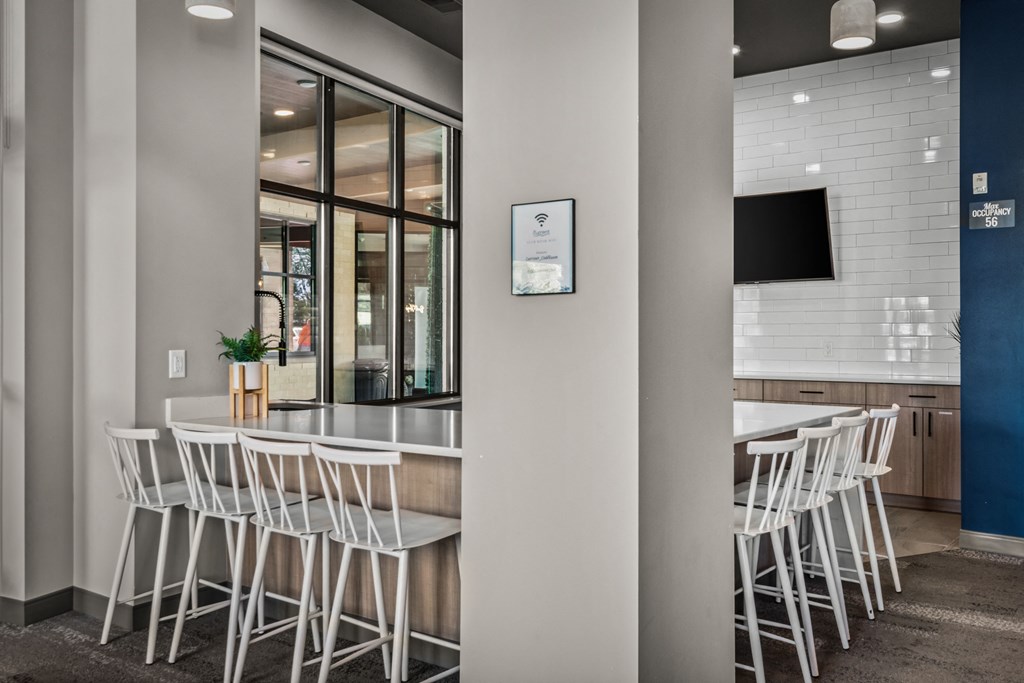 a communal area with white chairs in front of a bar and a television