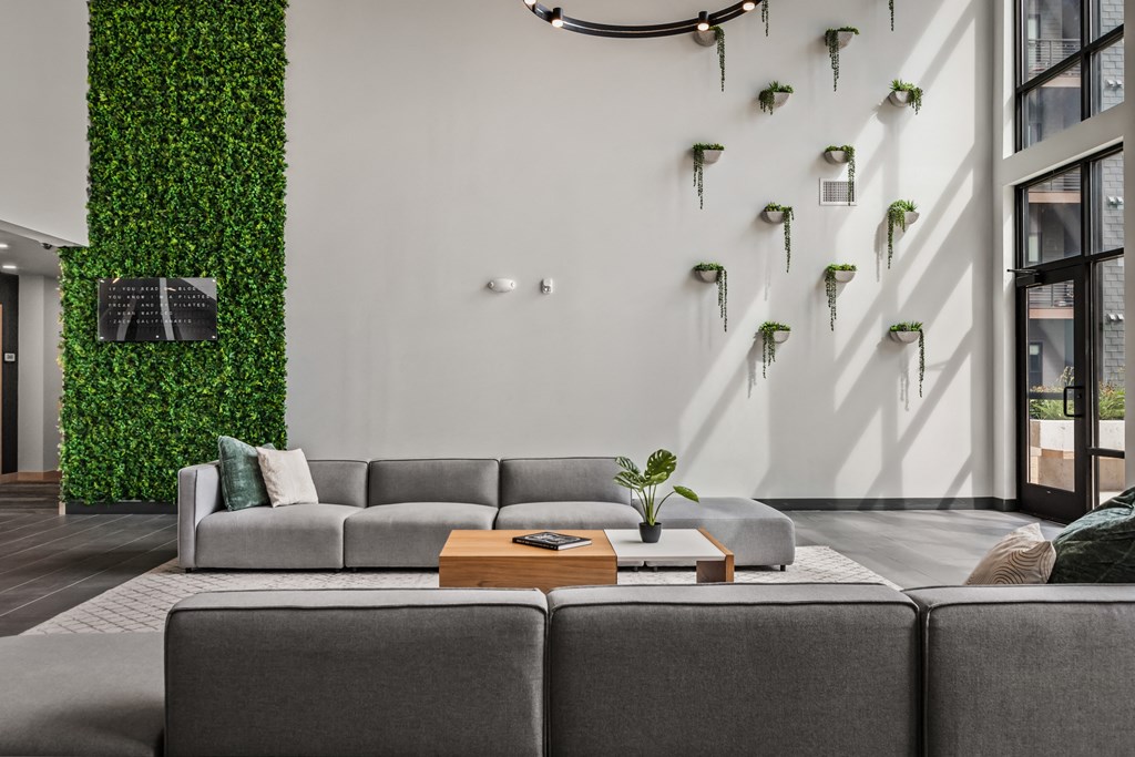 a living room with a white wall with plants on it and a gray couch